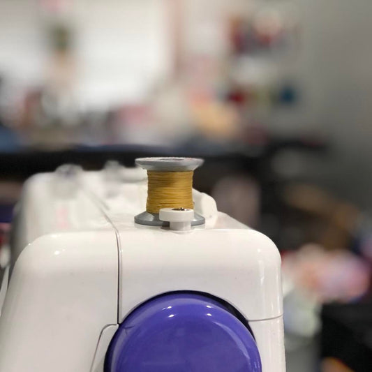 mustard colored spool of thread on top of a sewing machine