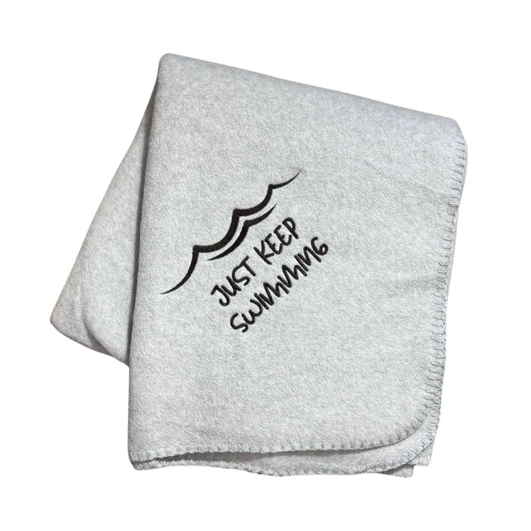 Gray blanket with 'Just Keep Swimming' text and wave design in black stitching