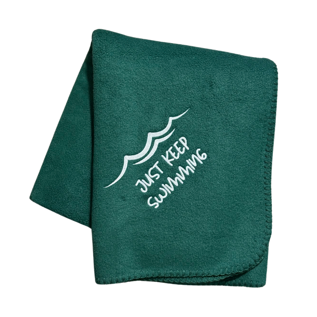 Green blanket with 'Just Keep Swimming' text in white embroidery