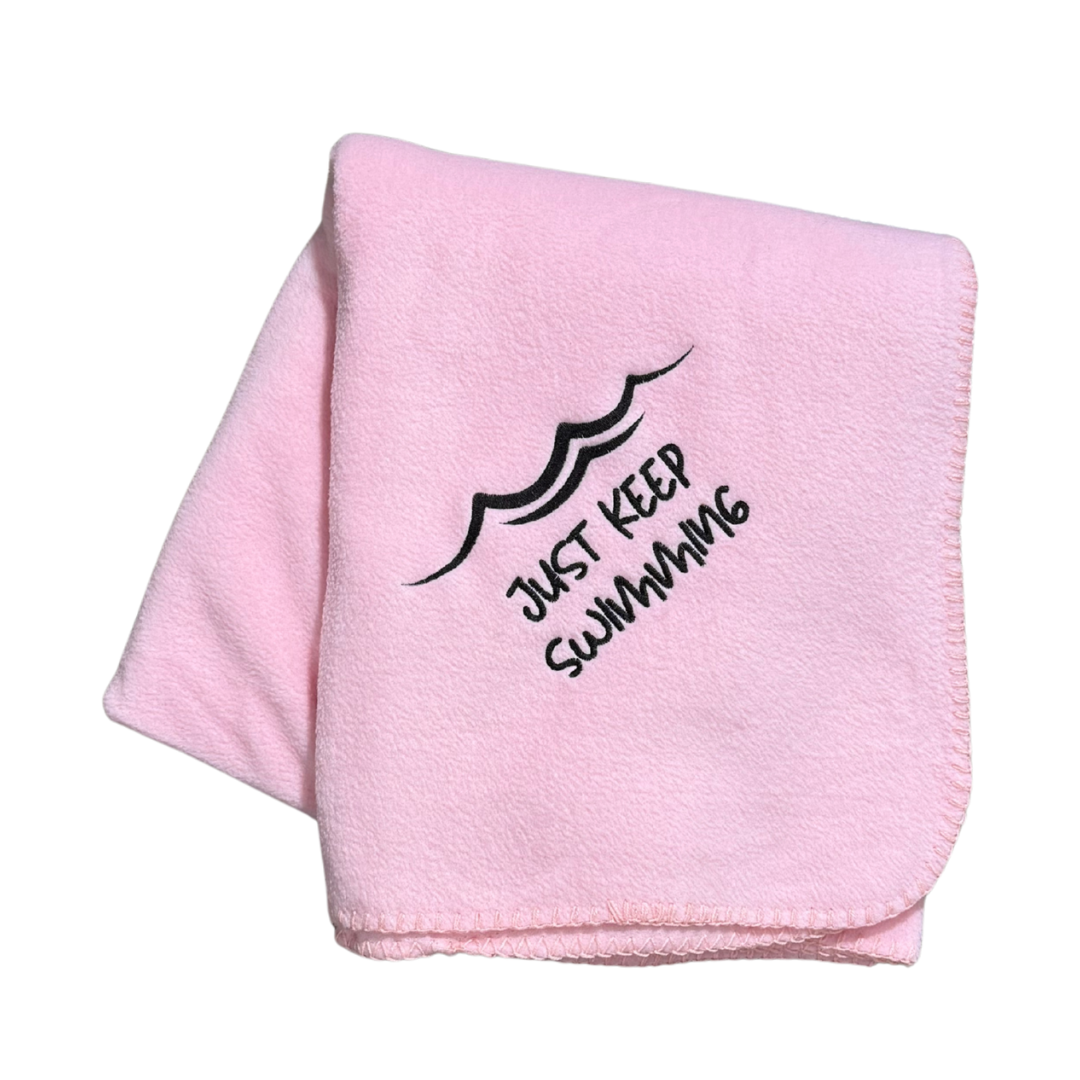 Pink blanket with 'Just Keep Swimming' text and wave design in black thread embroidery