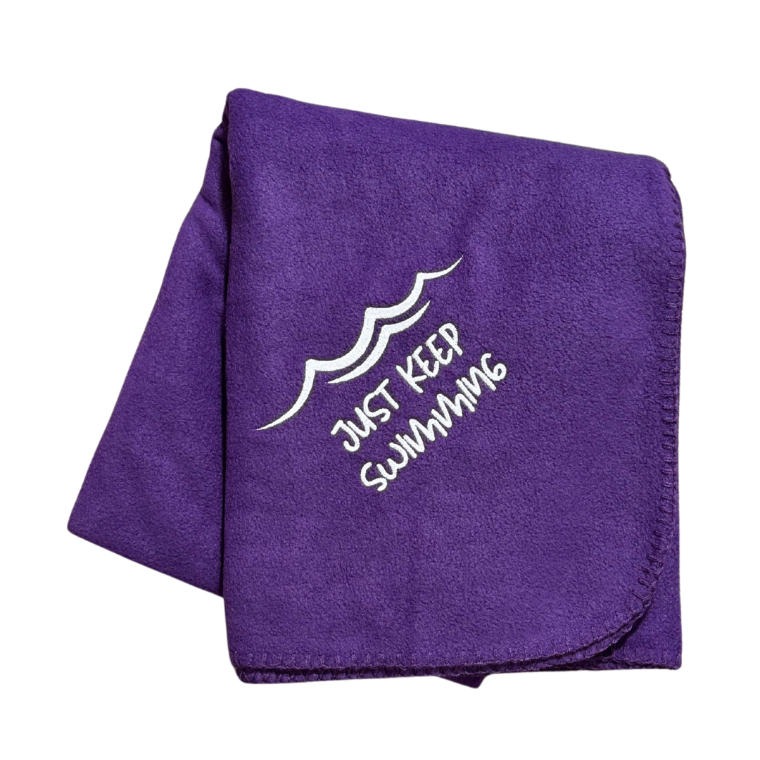 Purple blanket with 'Just Keep Swimming' text and wave design in white stitching