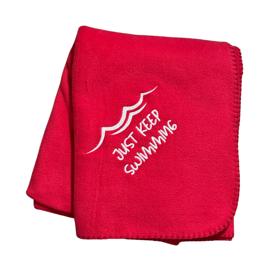 Red blanket with 'Just Keep Swimming' text and wave design in white embroidery