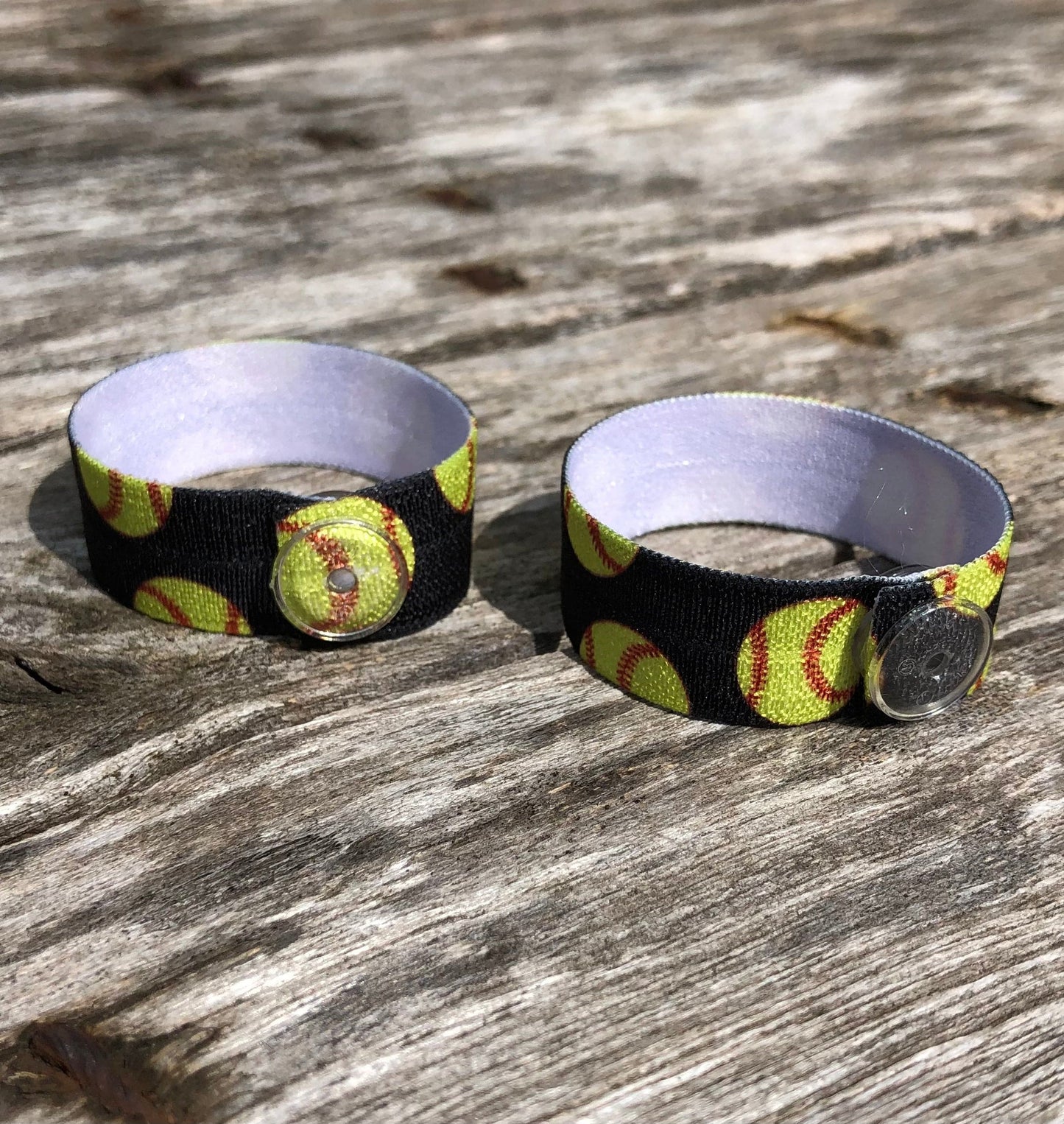 pair of black softball sleeve clips with random yellow softballs and clear snaps