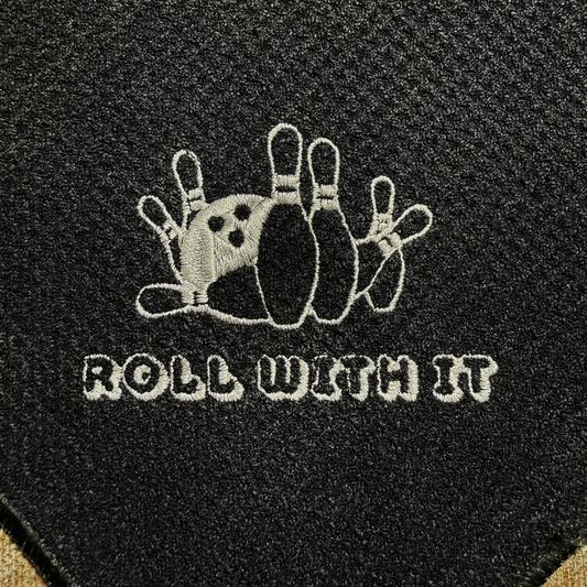 Black bowling ball with white embroidered design and 'Roll with It' text on a black background