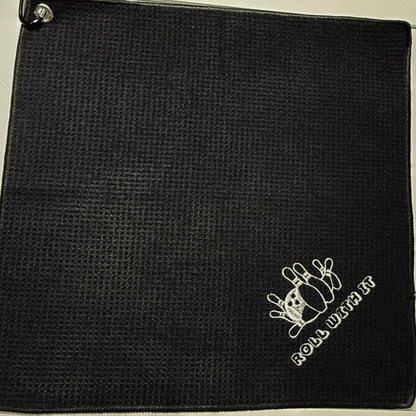 Black textured towel with 'Roll With It' logo embroidered in white thread.