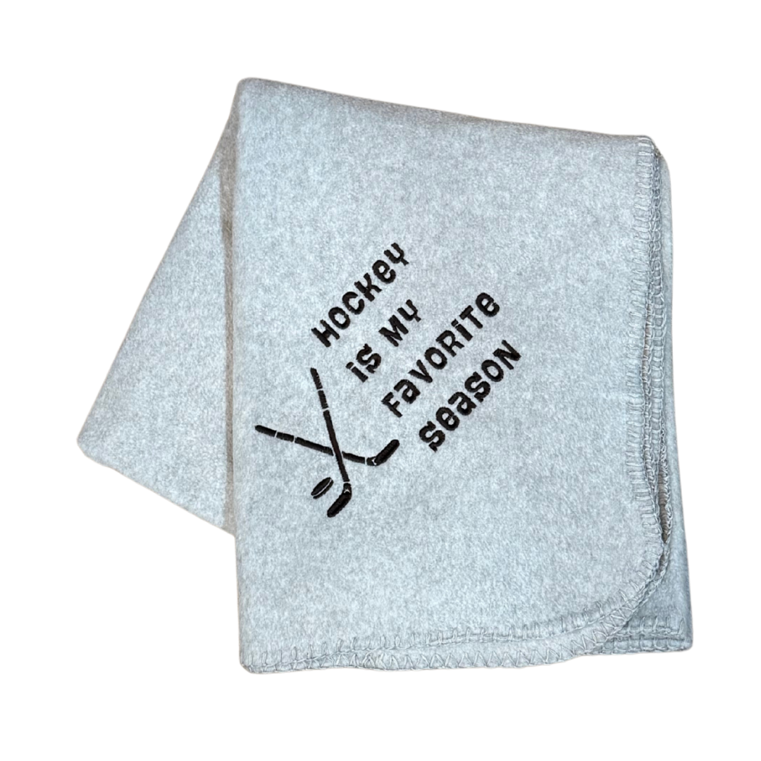 Gray blanket with 'Hockey is my favorite season' text and hockey stick graphics in black stitching