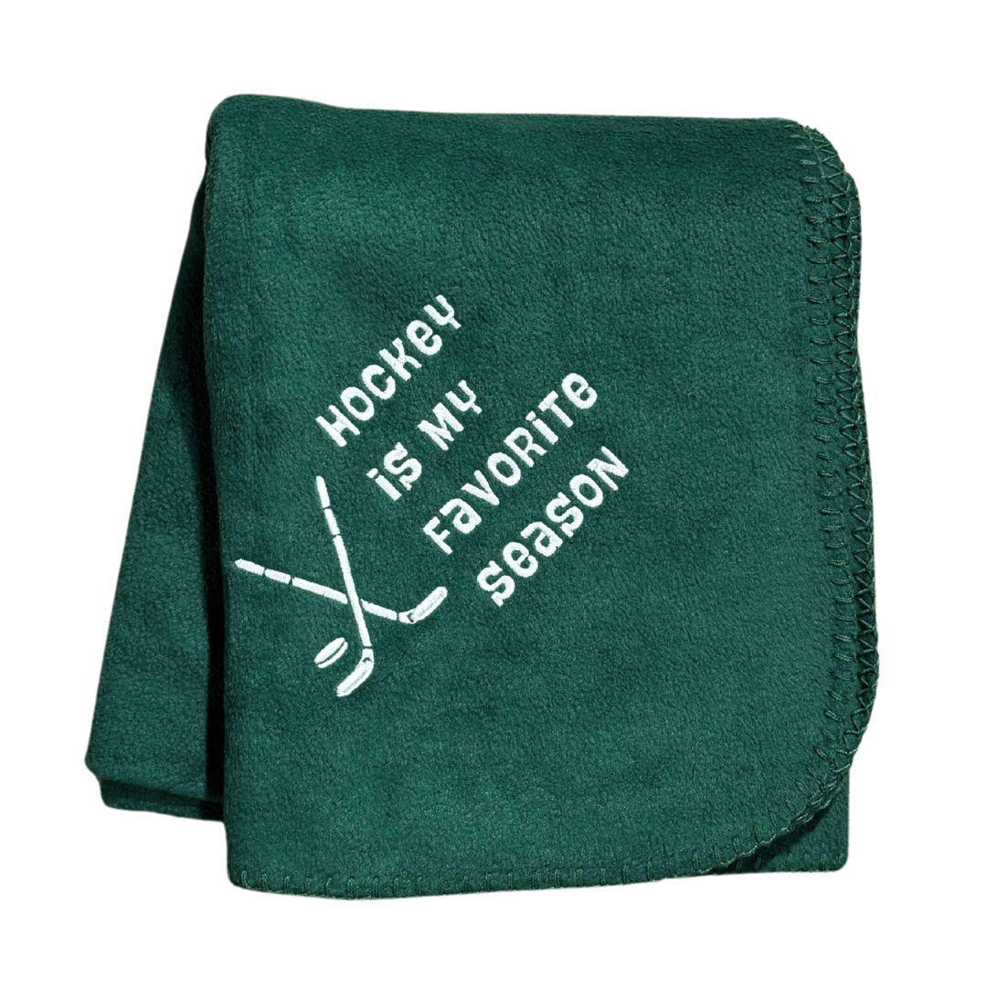 Green blanket with 'Hockey is my favorite season' text and hockey stick graphics in white