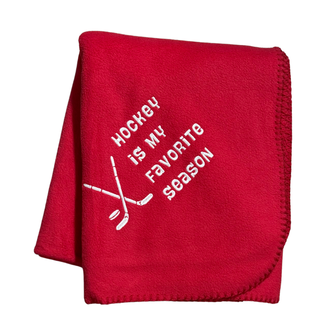 Red blanket with 'Hockey is my favorite season' text and hockey stick graphics in white stitching