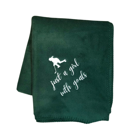 A green fleece blanket with hockey-themed embroidery and the phrase 'just a girl with goals' stitched in white