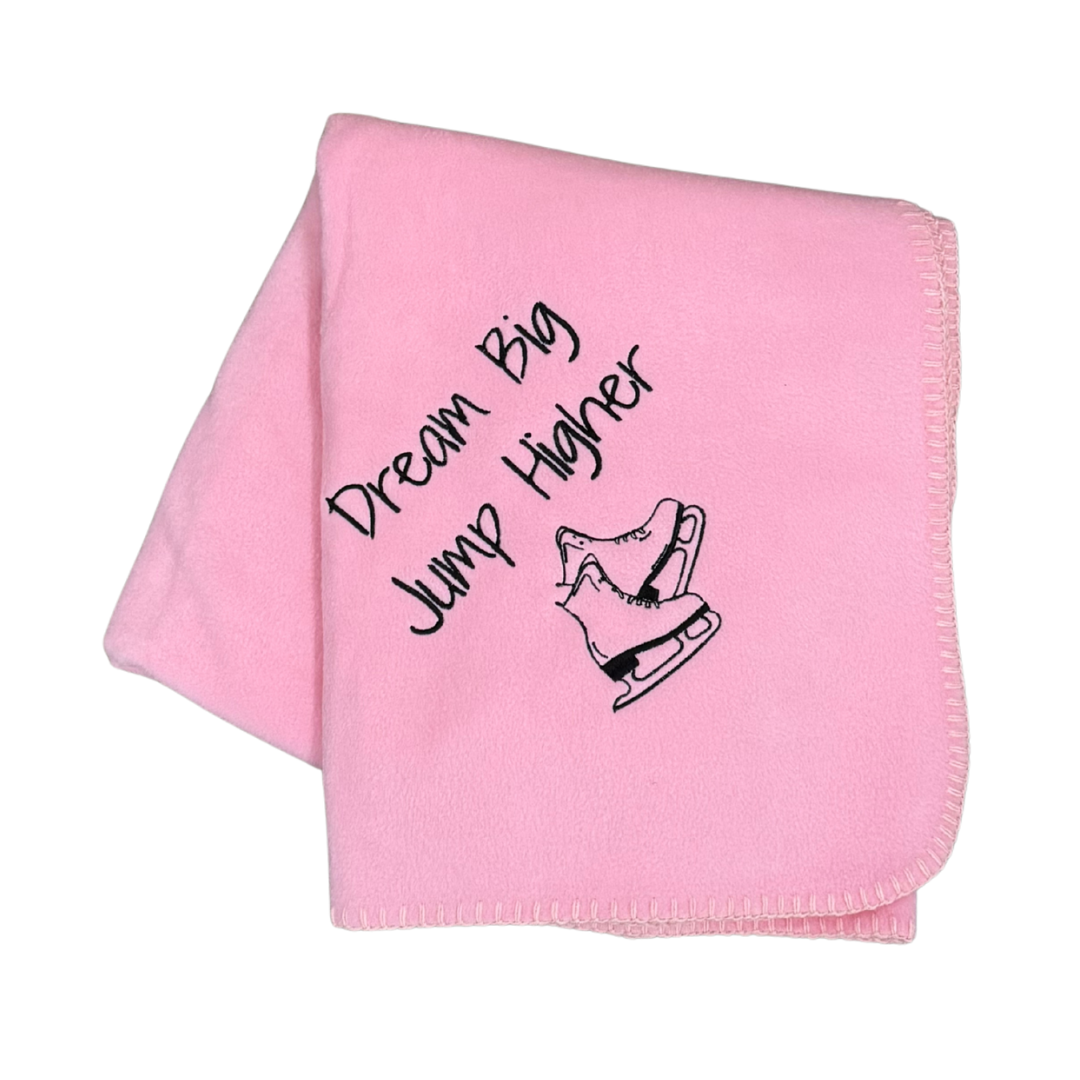 Pink blanket with 'Dream Big, Jump Higher' text and ice skate design in black embroidery