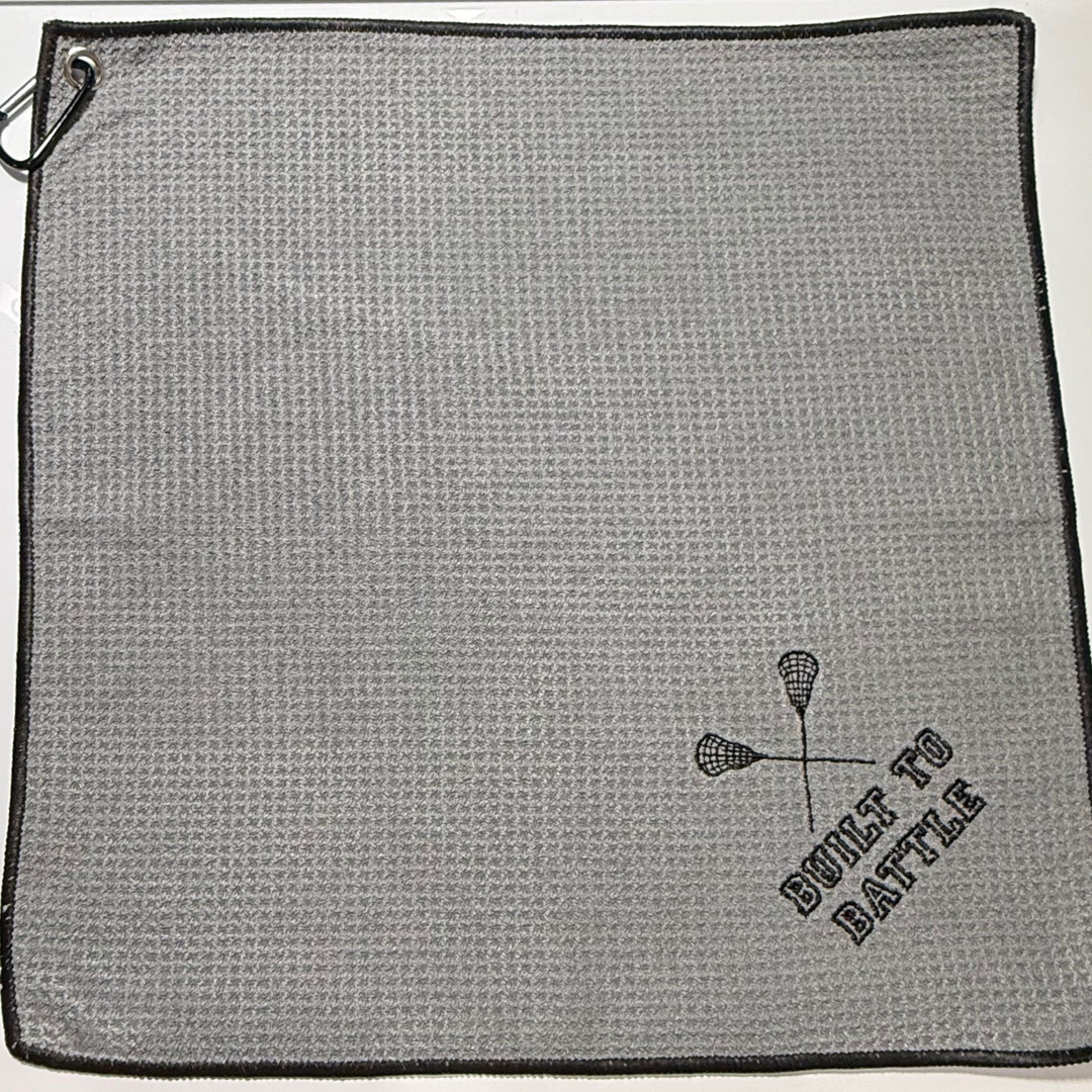 Gray towel with 'Built to Battle' and lacrosse design embroidery on a white background