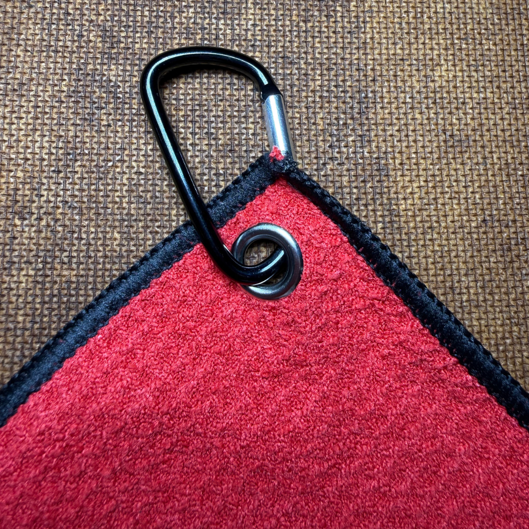 Red towel with black border and carabiner clip on a textured brown background