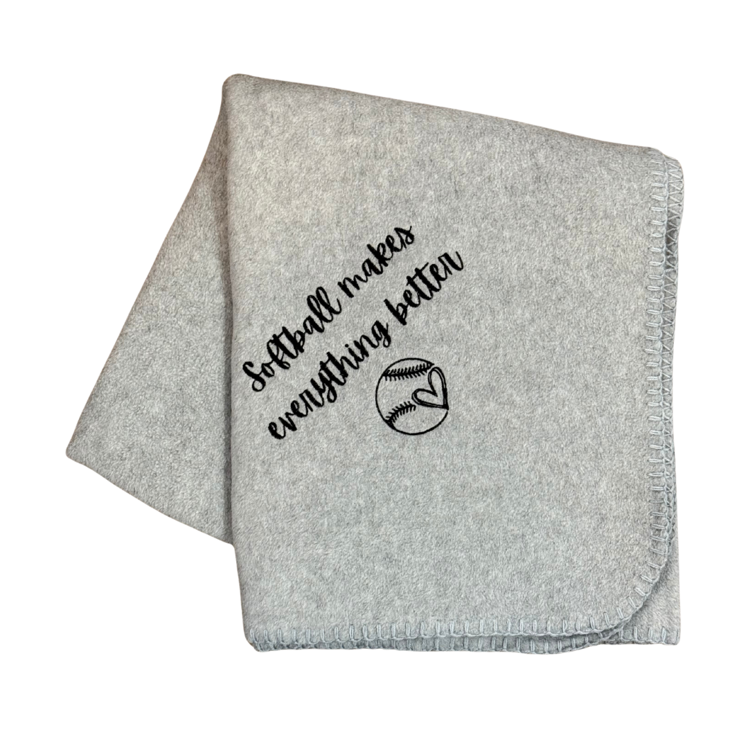 Gray blanket with 'Softball makes everything better' text and softball graphic in black stitching
