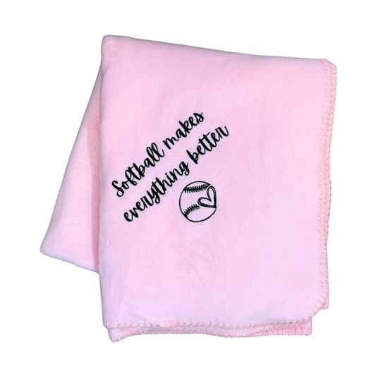 Pink blanket with 'Softball makes everything better' text and a softball graphic in black stitching